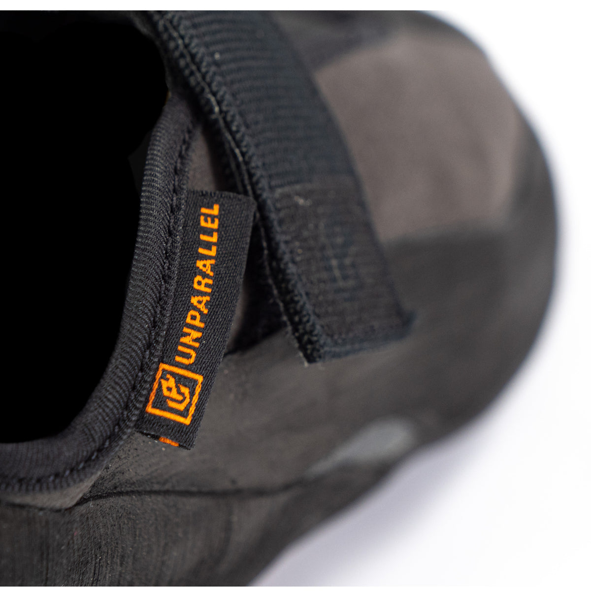 Unparallel logo in orange on a black tab with rest of shoe blurred out in background