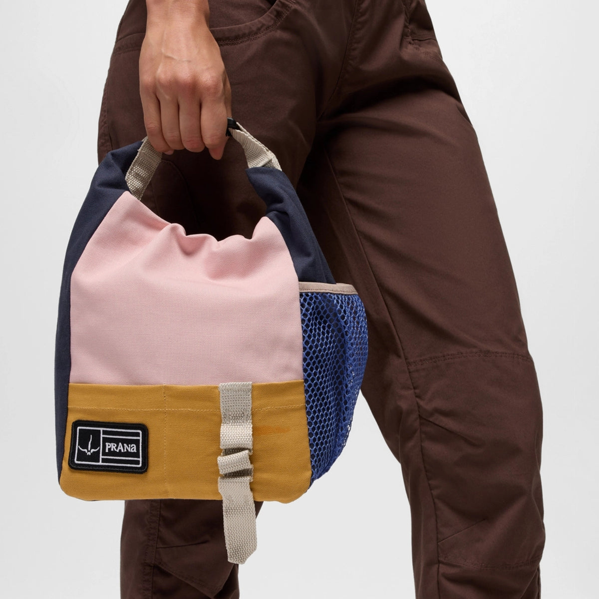 Person holding a colorful bag with a visible brand label on a plain background