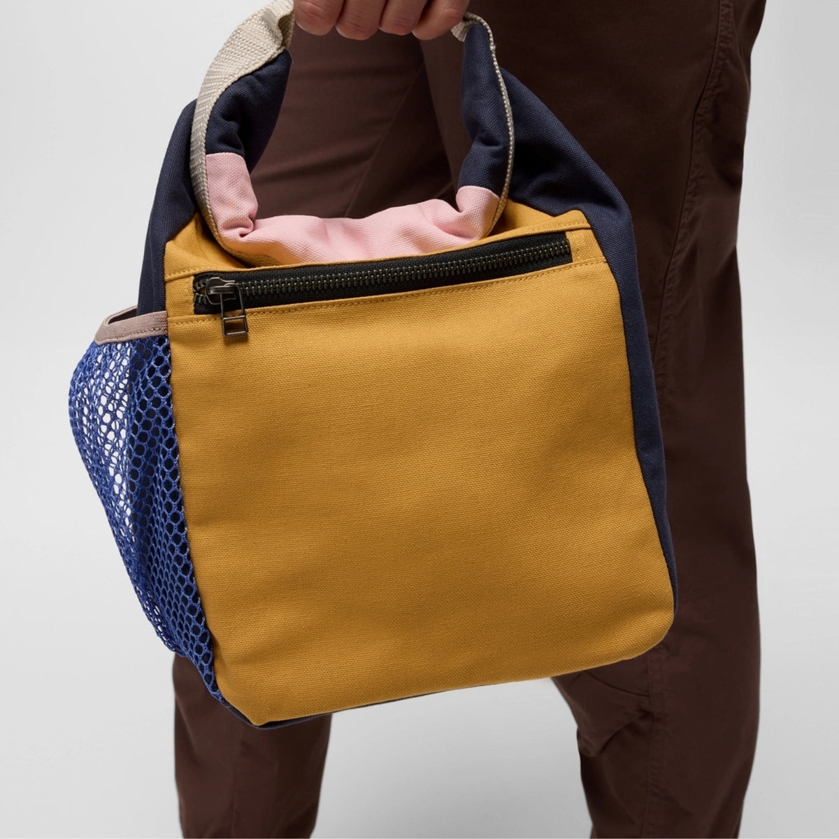 Yellow bag with blue mesh pocket held by a person against a light gray background