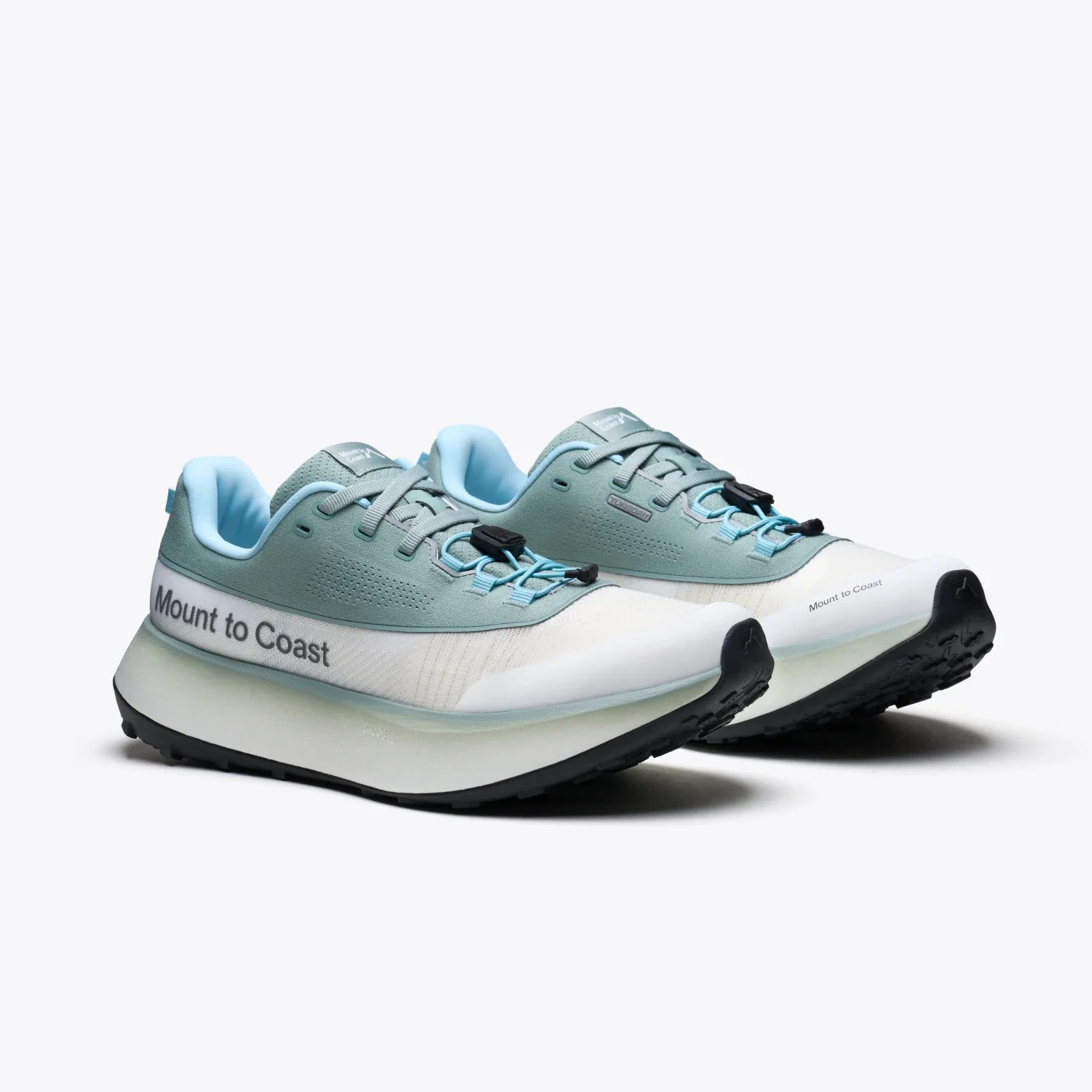 A single athletic trail running shoe from Mount to Coast, shown from a three-quarters angle on a light gray studio background. The shoe features a white mesh upper, a dusty blue suede overlay, light blue laces, a blue interior lining, and a thick white and translucent gray midsole with a black outsole.