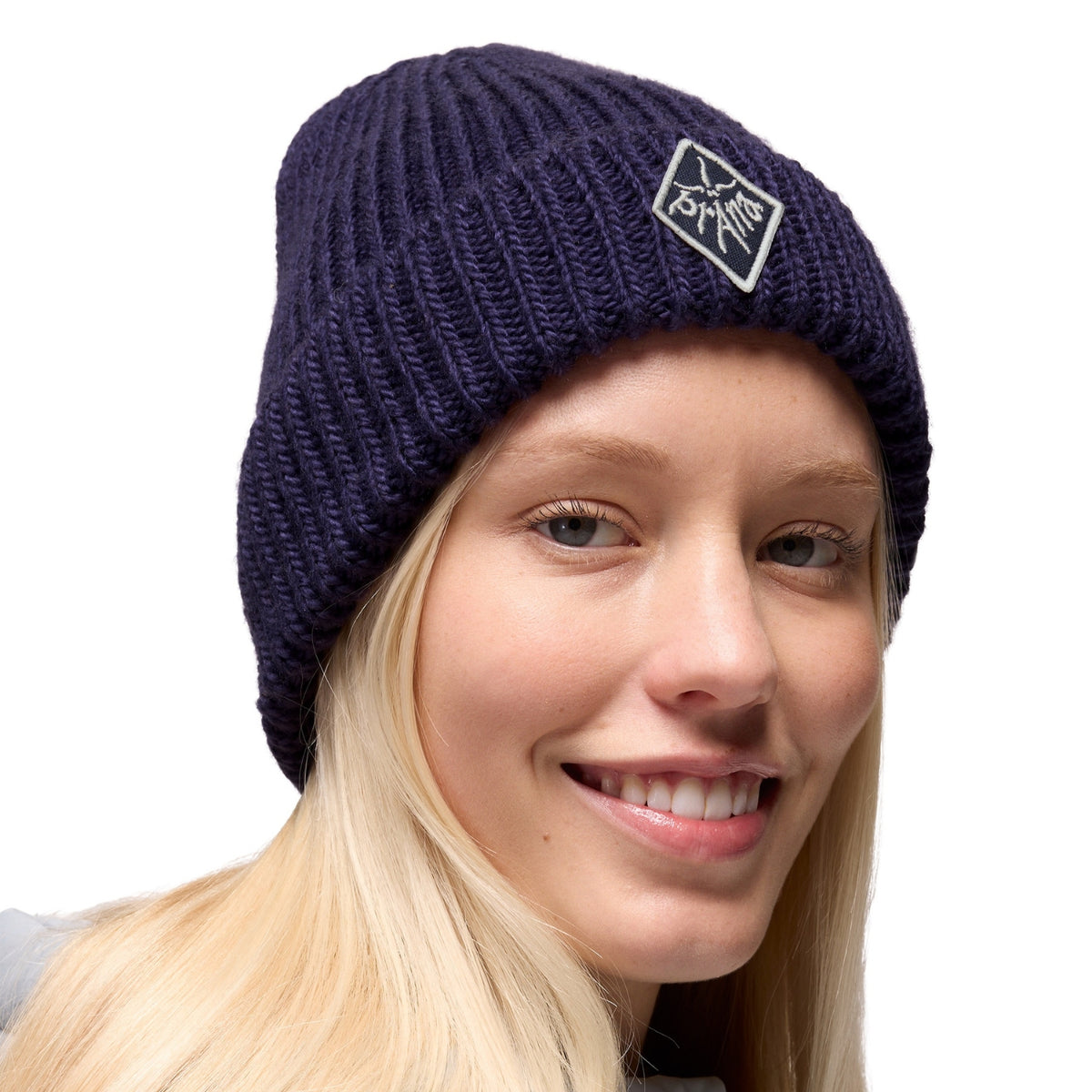 Person wearing a navy blue knit beanie with a logo on a white background