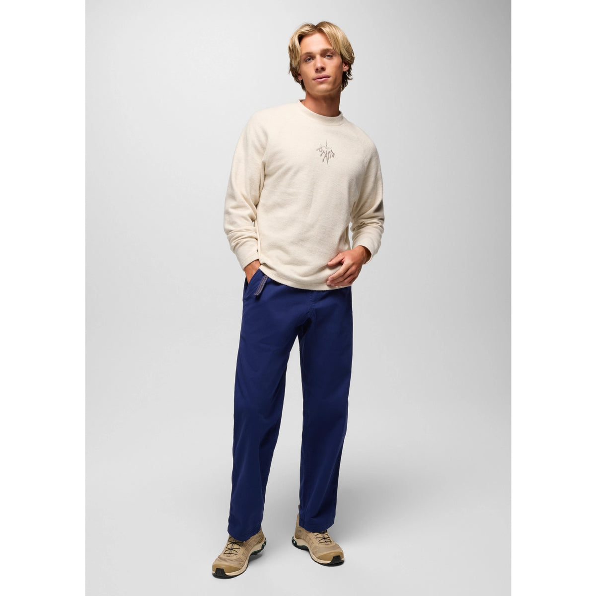 Man wearing a beige sweater and blue pants on a gray background