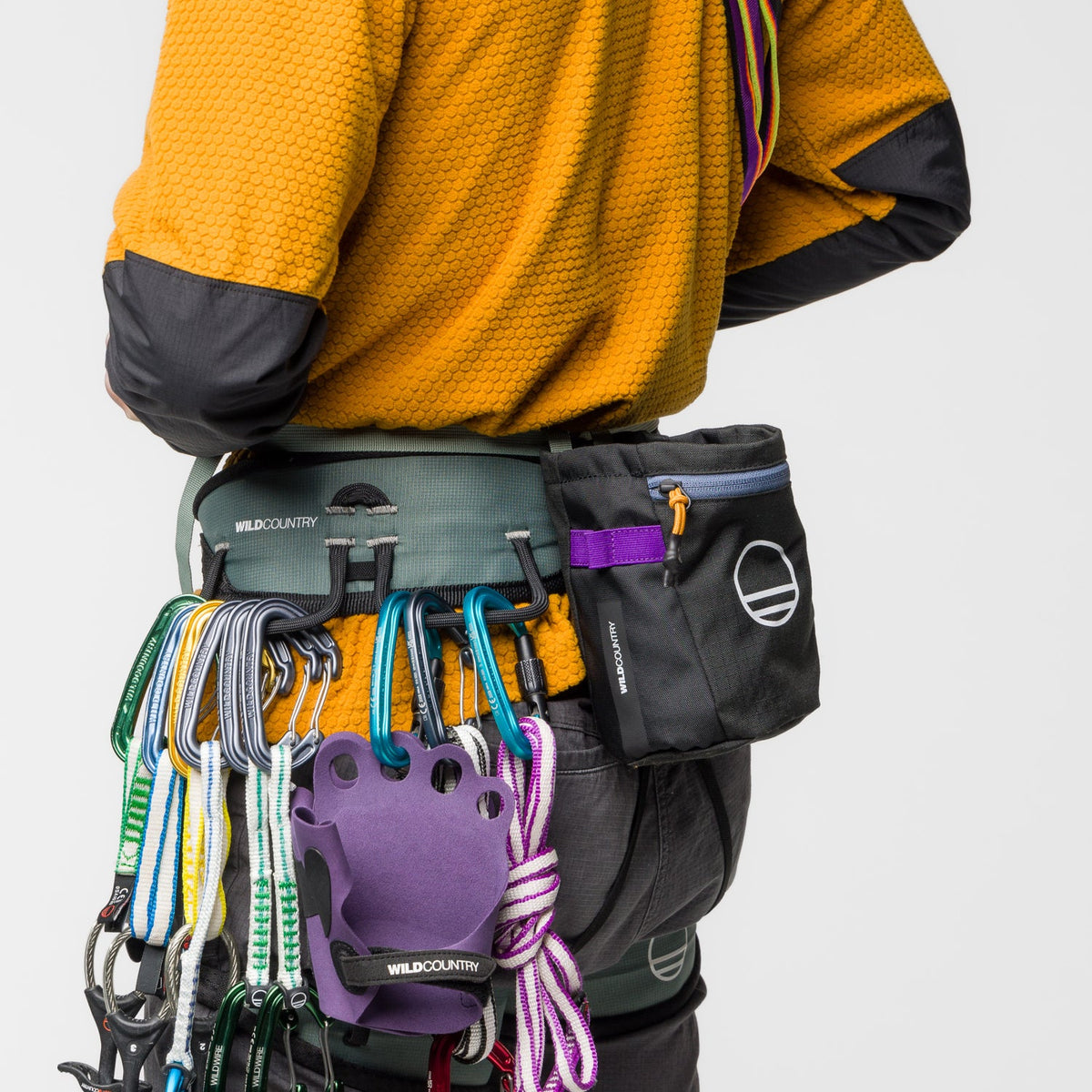 Person wearing a climbing harness with climbing gear on a plain background