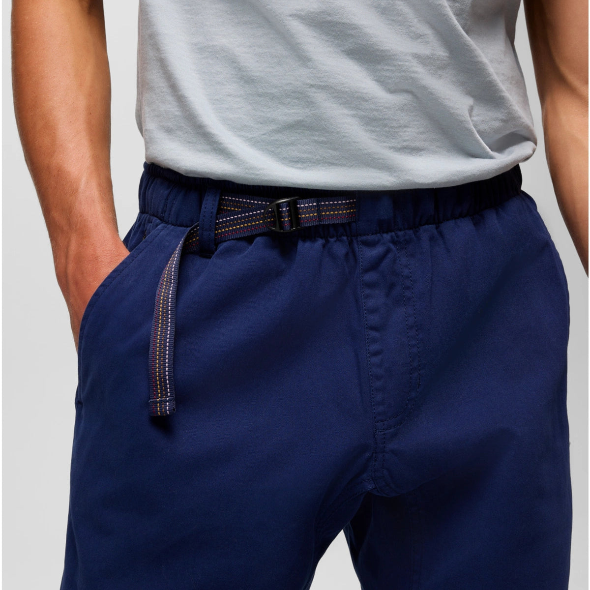Person wearing navy pants with a belt on a plain background