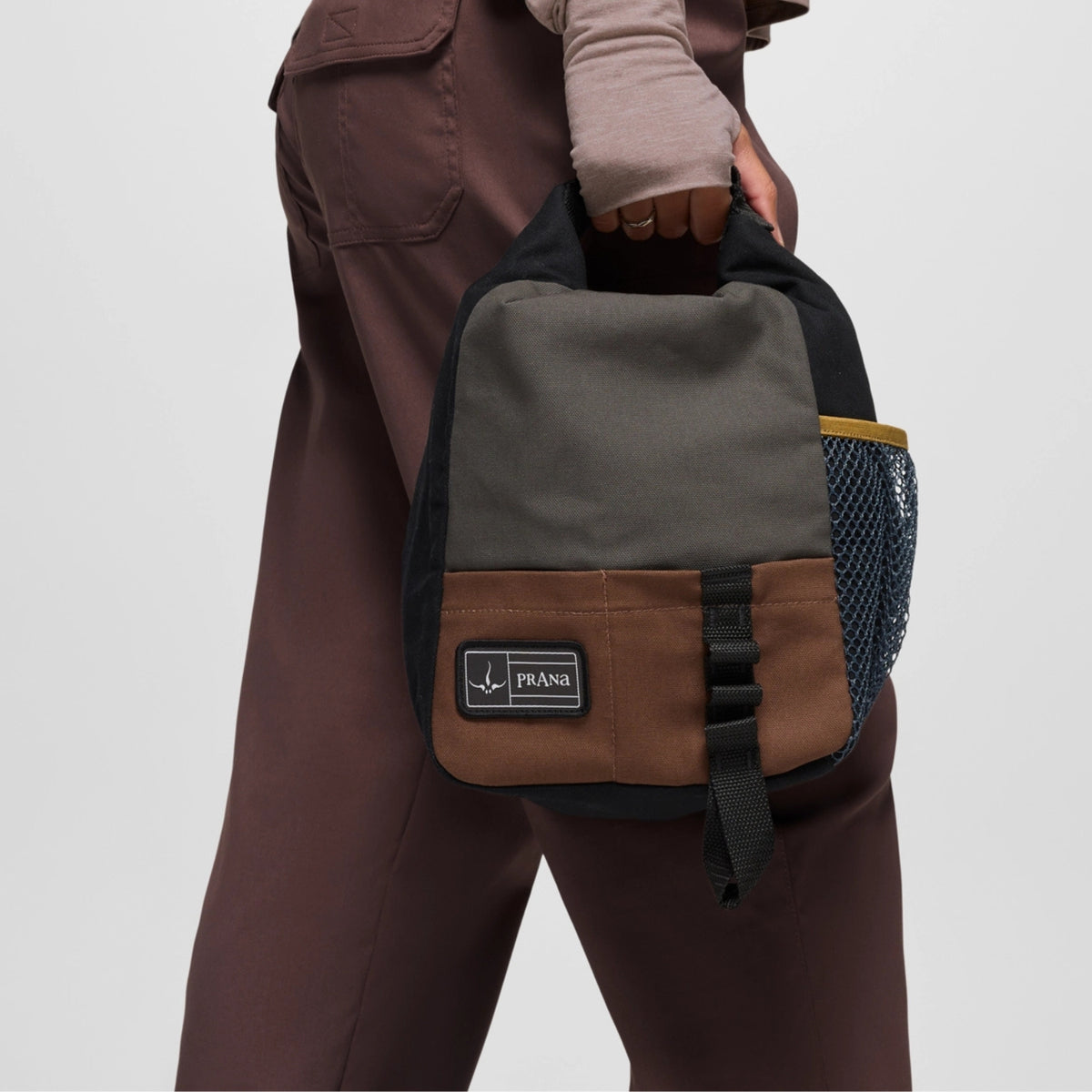 Person holding a gray and brown backpack with Prana logo on a light gray background