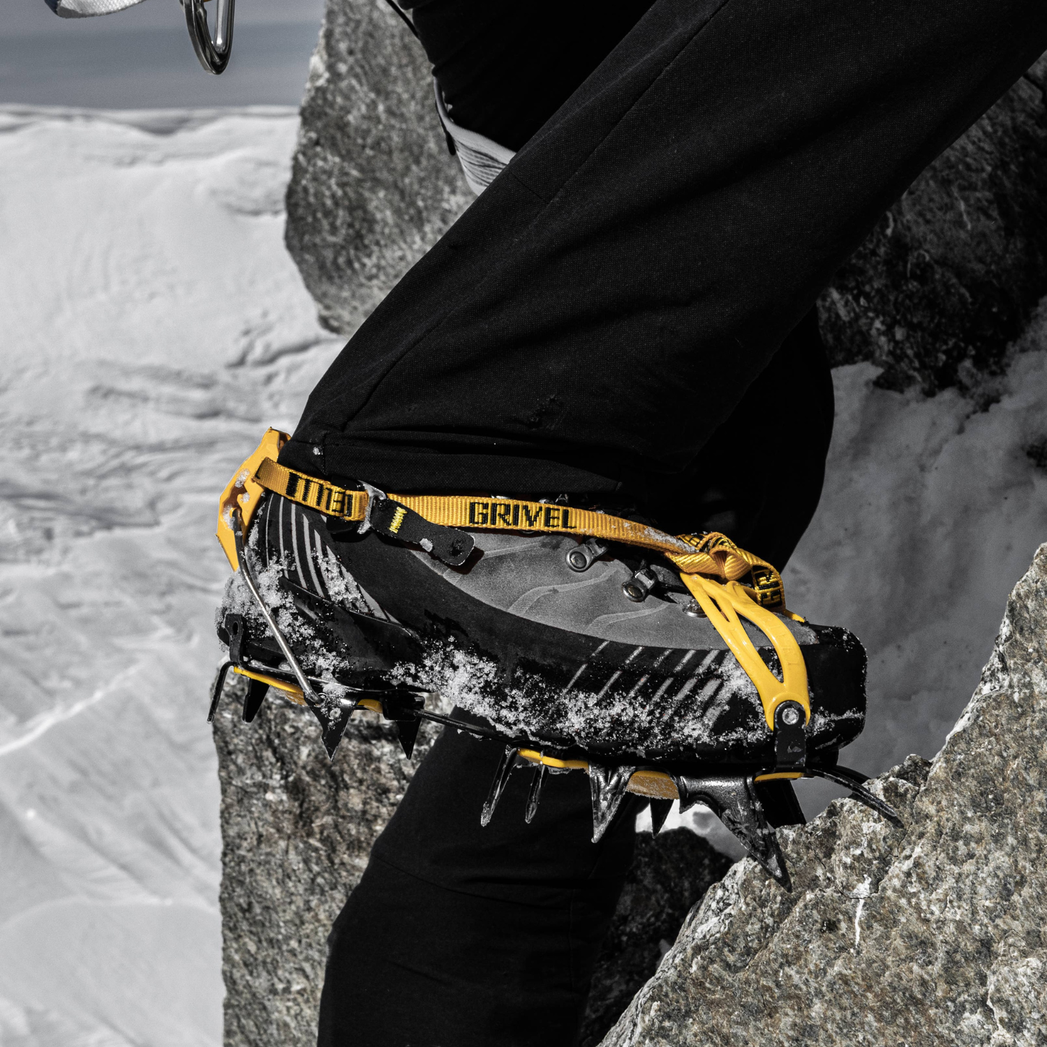 Black and yellow ice climbing crampons with a yellow strap featuring black branding, shown on a light gray background.