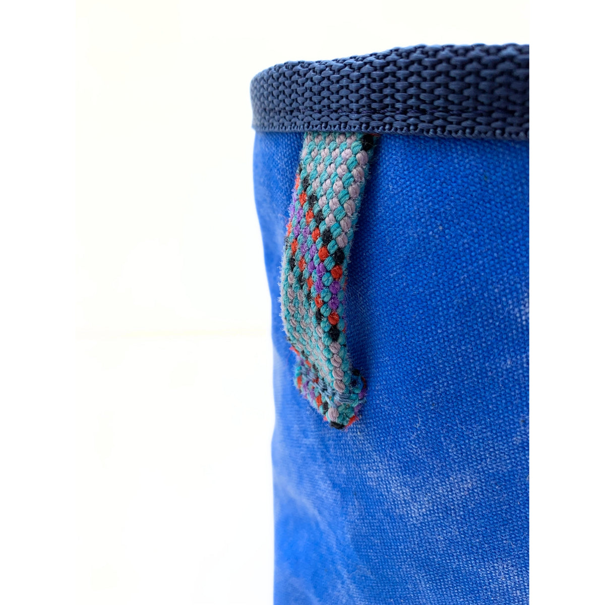 Blue fabric bag with a colorful woven handle on a white background