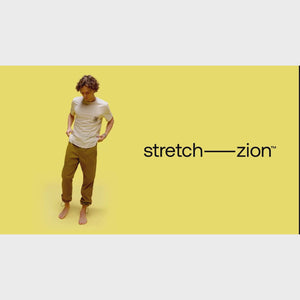 Man wearing Prana Stretch Zion Pull On Shorts for men in brown, standing barefoot against yellow background. Durable, UPF 50+ shorts with 2-way stretch.